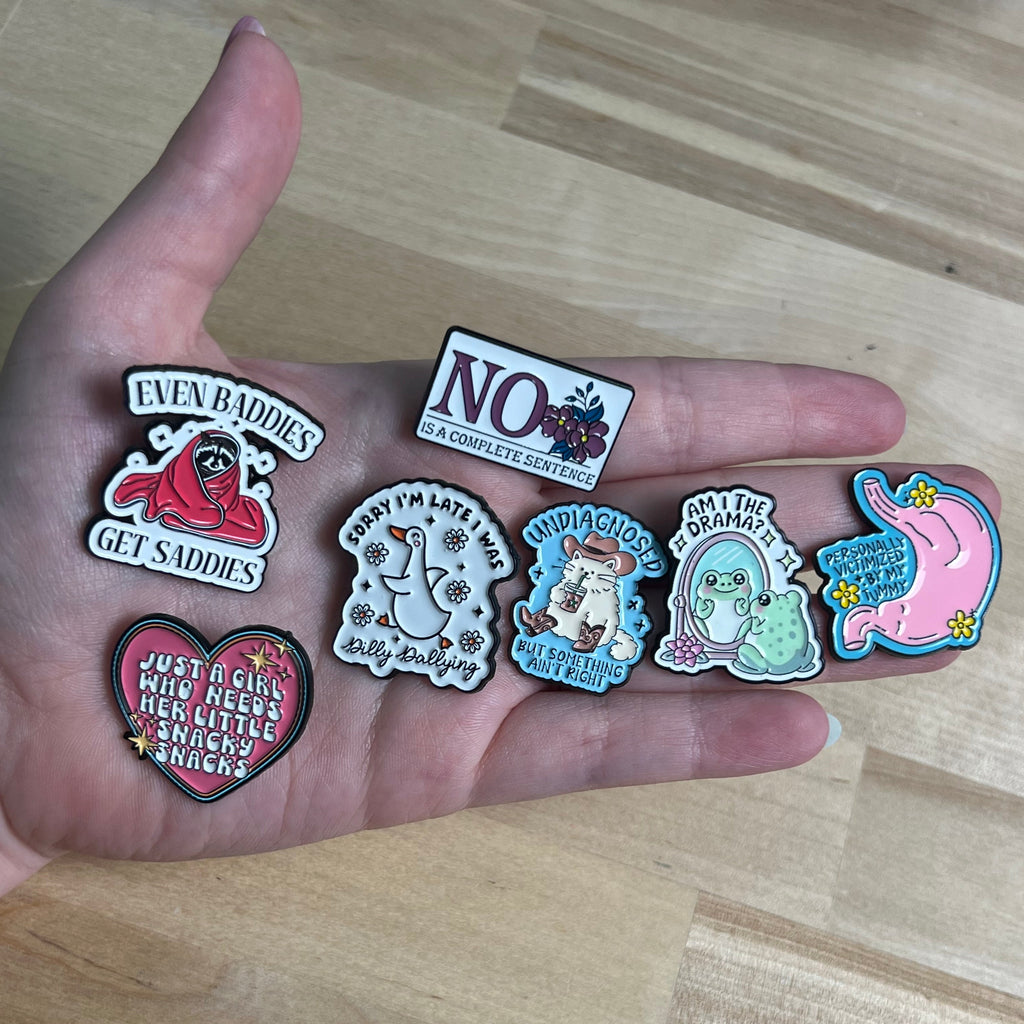 Hand holding various small decorative pins on a wooden surface