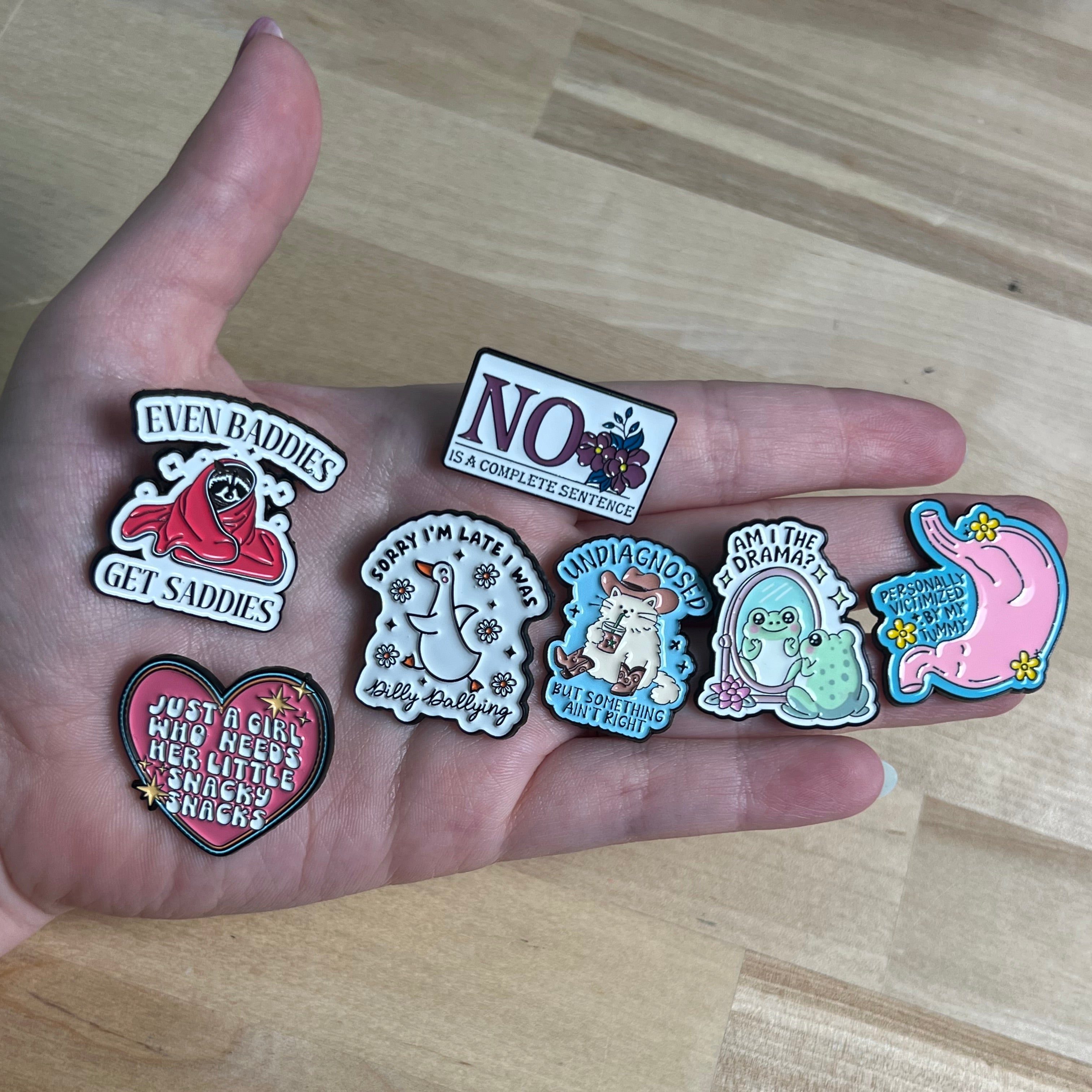 Hand holding various small decorative pins on a wooden surface