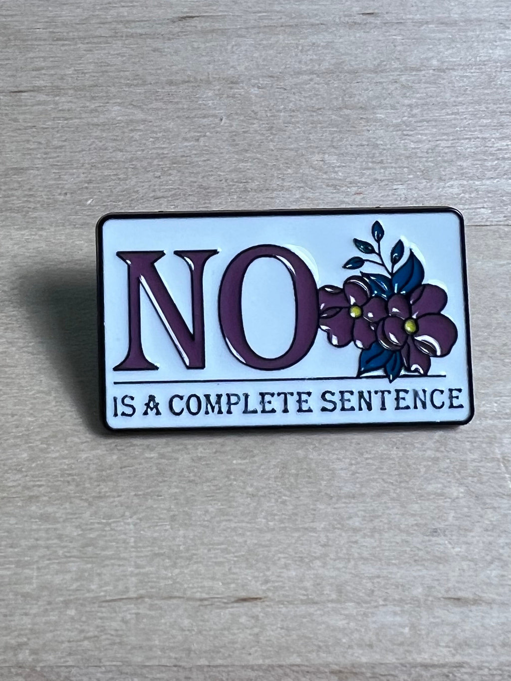 Enamel pin with floral design and text on a wooden surface