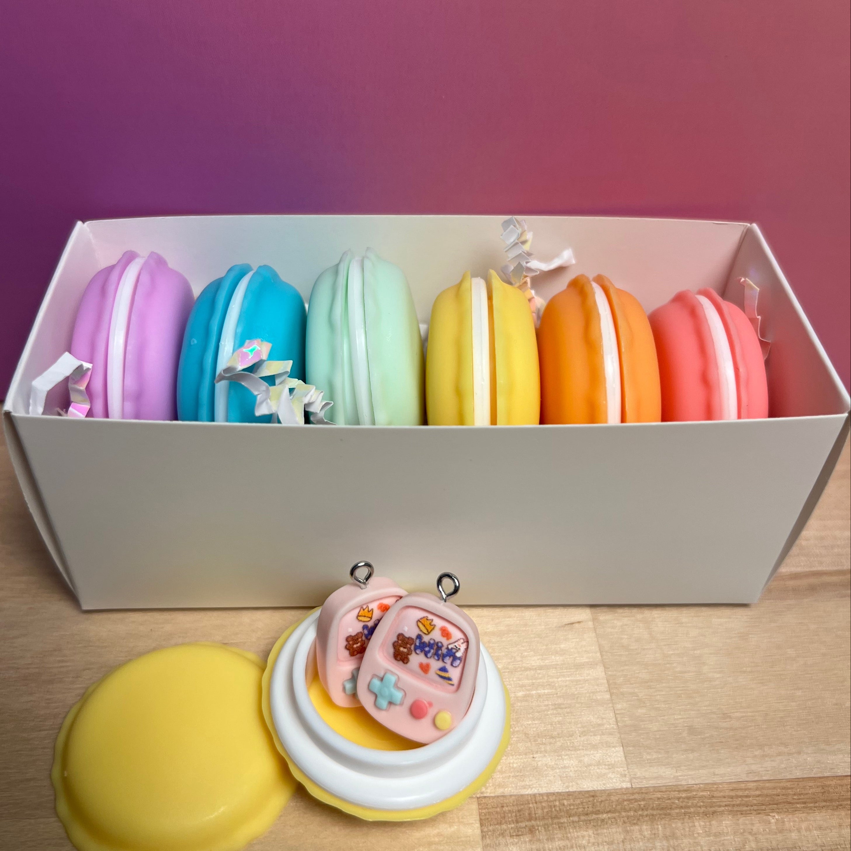 Colorful macaron-shaped containers stacked in a box with decorative items on a wooden surface.